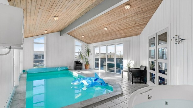 An indoor swimming pool with a dolphin float, wooden ceiling, and large windows. - Pet friendly home in Vestervig with sauna (Vestervig)