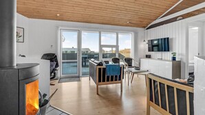 A modern interior with a wood-paneled ceiling, a fireplace, a dining area, and a kitchen with a TV. - Pet friendly home in Vestervig with sauna (Vestervig)