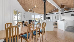 A spacious dining area with wooden chairs and a large table, a kitchen with modern appliances, and a high ceiling with exposed beams. - Pet friendly home in Vestervig with sauna (Vestervig)