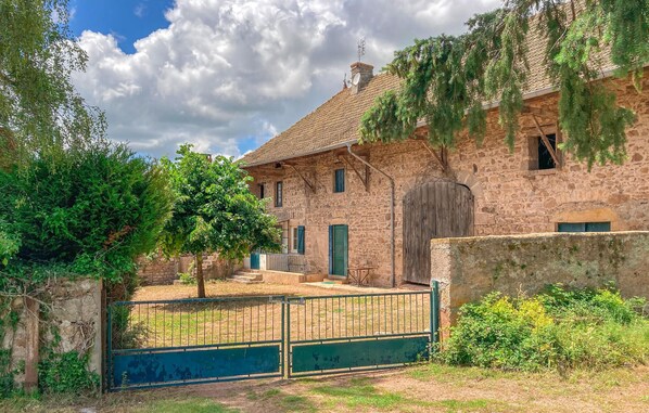 Ein rustikales Steinhaus mit Ziegeldach, einem hölzernen Tor und üppiger Bepflanzung.