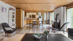 Een moderne woonkamer met een zwarte leren fauteuil, een houten eettafel en een zwarte bank. Er is een keuken met een fornuis en een boekenkast.