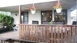 Eine Holzterrasse mit Geländer, einer Bank und hängenden Blumentöpfen.