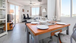 A modern dining area with a wooden table set for two, a television, and a kitchen area in the background. - Nice apartment in Riviera del Sol (Riviera del Sol)