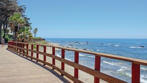 A wooden boardwalk with red railings leading to a beach with palm trees and ocean waves. - Nice apartment in Riviera del Sol (Riviera del Sol)