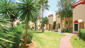A courtyard with palm trees, a red pathway, and buildings with red accents and balconies. - Nice apartment in Riviera del Sol (Riviera del Sol)
