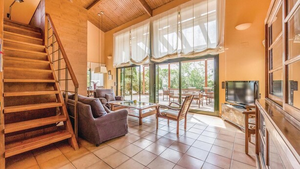 A spacious living room with a wooden staircase, large windows, and a TV. - Beautiful home in Capmany (Capmany)
