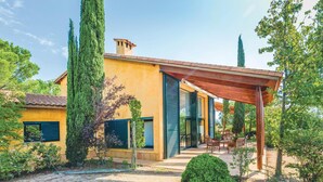 A modern house with a yellow facade, a covered patio with outdoor furniture, and tall trees surrounding the property. - Beautiful home in Capmany (Capmany)