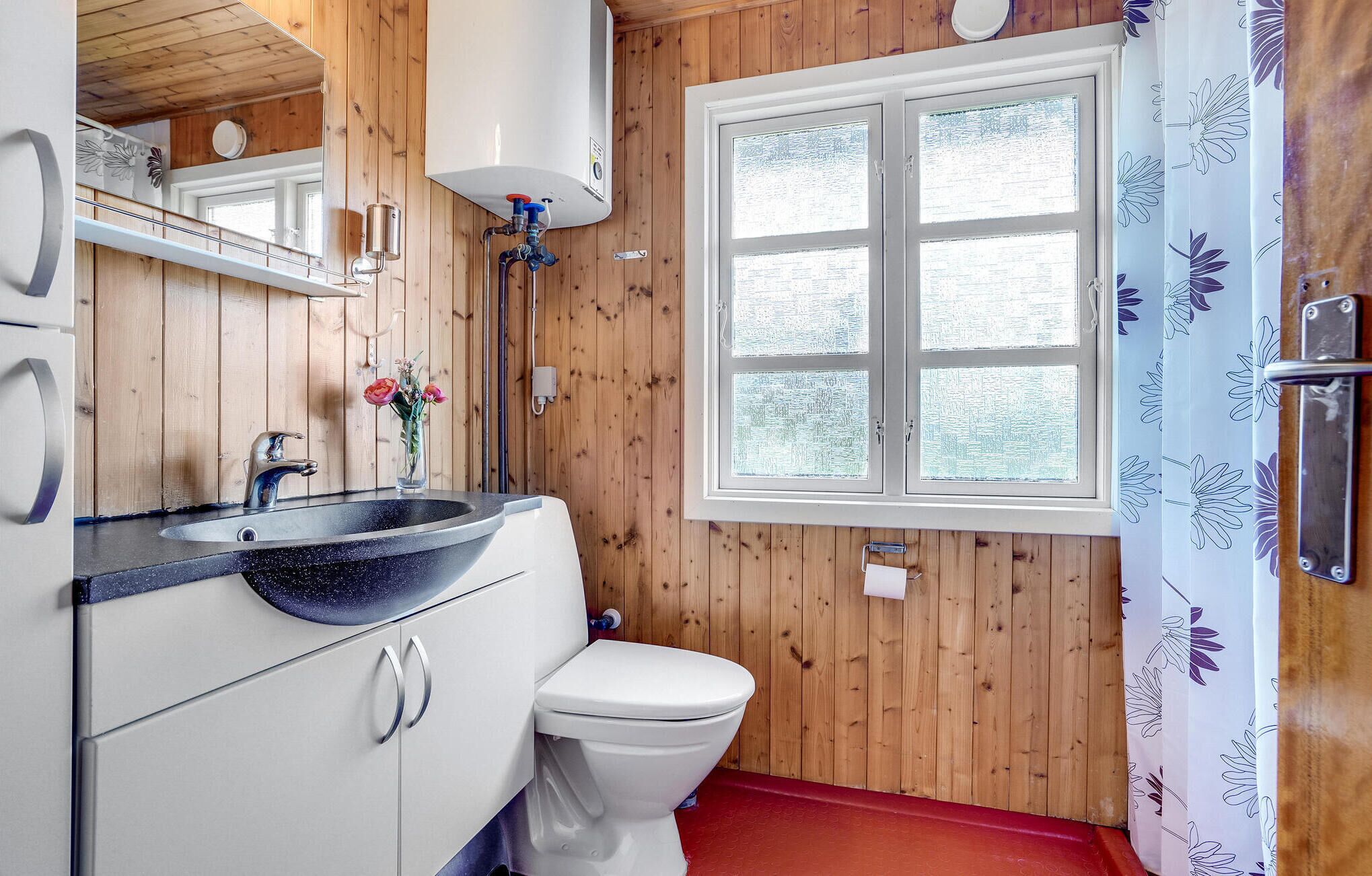 A wooden-paneled bathroom with a white toilet, a black sink with a round basin, and a window with frosted glass.