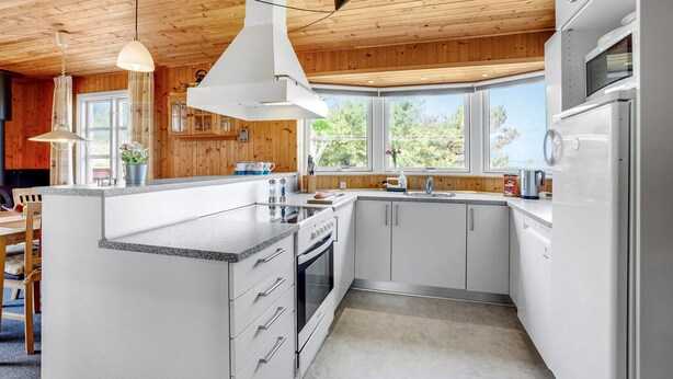 A modern kitchen with white cabinets, a granite countertop, and a built-in oven. There are large windows providing natural light and a view of greenery outside. - Cozy home in Frøstrup with sauna (Frøstrup)