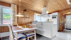 A wooden interior with a dining table, chairs, and a kitchen area including a refrigerator and microwave. - Cozy home in Frøstrup with sauna (Frøstrup)