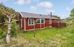 Une maison en bois rouge, avec un toit en pente, des fenêtres à cadre blanc et une cheminée.