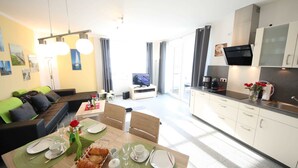 Un salon moderne comprenant un coin repas, une cuisine et un téléviseur en arrière-plan.