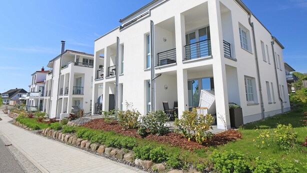 Un immeuble résidentiel moderne à deux étages, doté de balcons, d’une allée pavée et de jardins aménagés.
