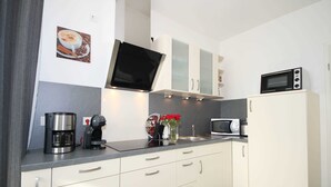 Une cuisine moderne avec des meubles blancs, une machine à café, un four à micro-ondes et un téléviseur fixé au-dessus du plan de travail.