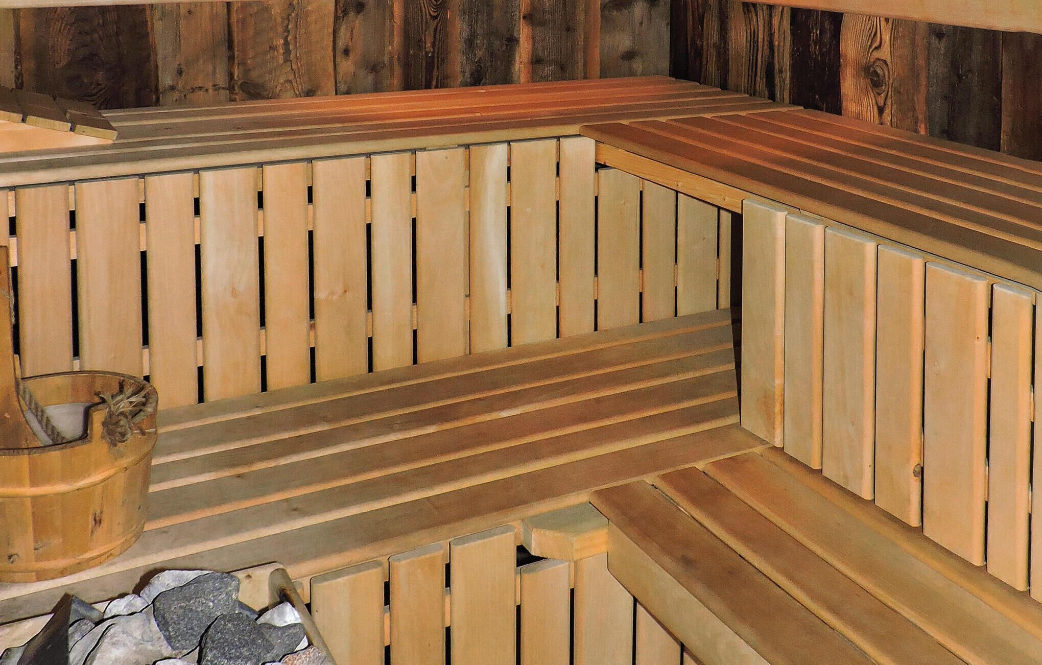 Una panca in legno per sauna dalla forma sinuosa, una conca in pietra e una panca in legno con schienale a listelli.