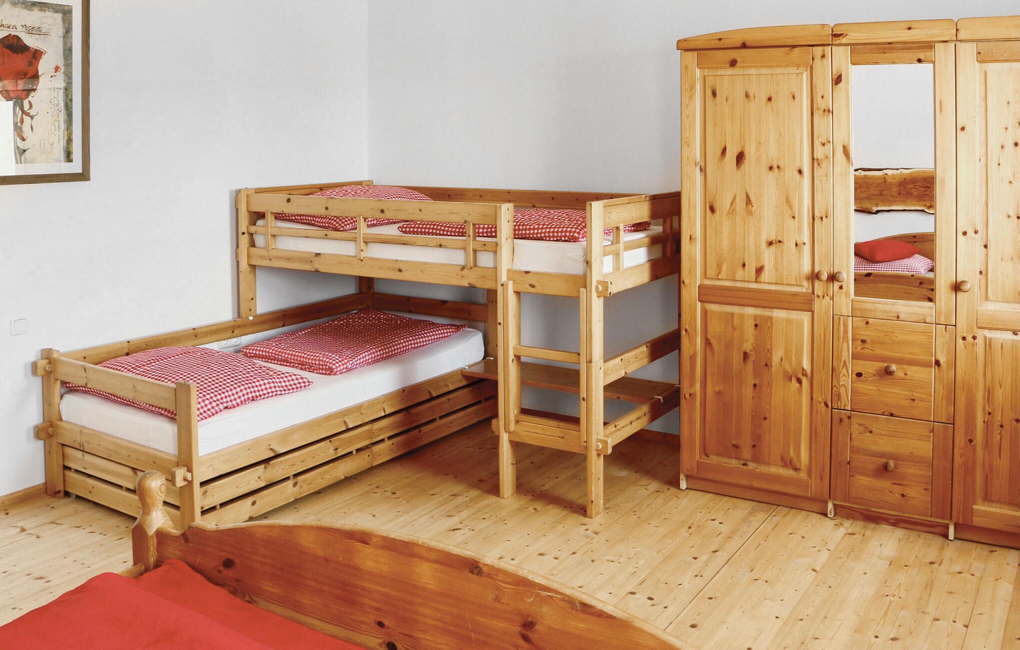 A bunk bed with a wooden wardrobe and a small bench.