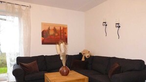 A living room with a dark-colored sofa, a wooden coffee table, and a painting on the wall. - Semi-detached house / Sonnenstrand No. 5 - Glowe - Semi-detached house Sonnenstrand / (Glowe)