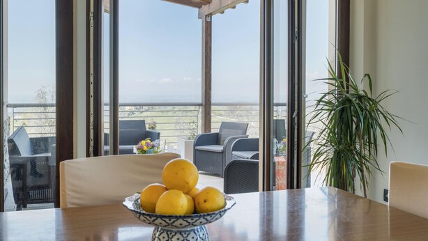 A dining area with a table, a bowl of lemons, wicker chairs, and a view of the outdoors. - Lovely home in Collevecchio (RI) with sauna (Collevecchio (RI))
