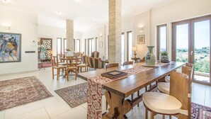 A spacious dining area with a long wooden table, multiple chairs, and a view of the outdoors through large windows. - Lovely home in Collevecchio (RI) with sauna (Collevecchio (RI))