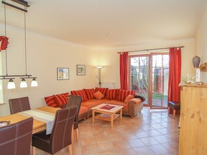 Een woonkamer met een bank, stoelen, een tafel en uitzicht door een glazen deur.