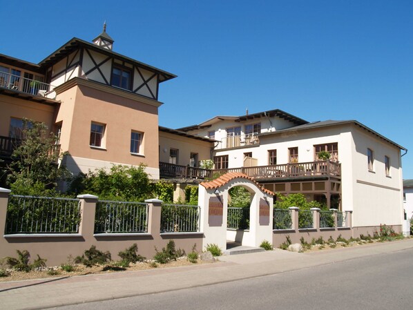 A multi-story residential building with balconies, a gated entrance, and a clear sky.