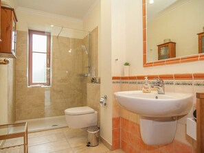 Een badkamer met douche, toilet, wastafel en spiegel.