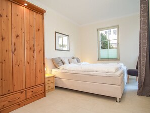 Een slaapkamer met een bed, een houten garderobe, een nachtkastje en een raam met jaloezieën.