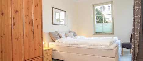 A bedroom with a bed, a wooden wardrobe, a bedside table, and a window with blinds.