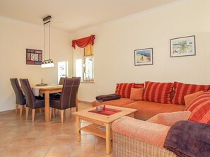 Un salon comprenant un canapé, des fauteuils, une table à manger et une fenêtre avec des rideaux.
