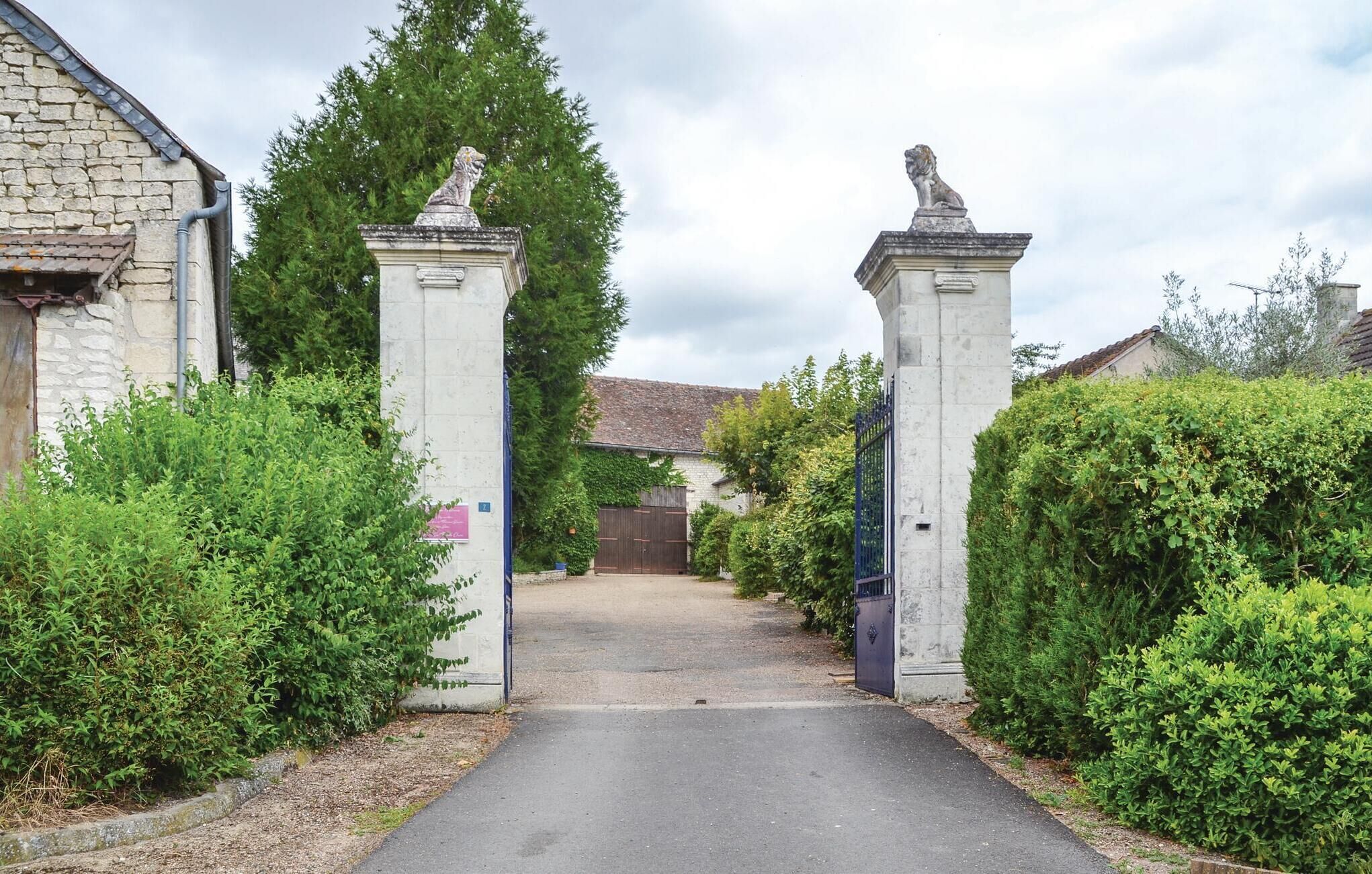 Une entrée fermée par un portail, avec des piliers en pierre et un chemin menant à un bâtiment.