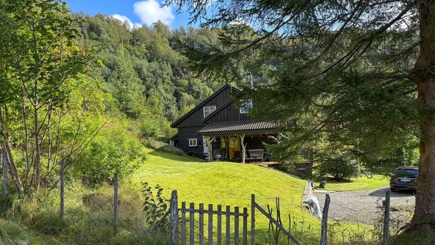 A wooden cabin with a porch, surrounded by lush greenery and a fence. - 5 bedroom amazing home in Matre (Matre)