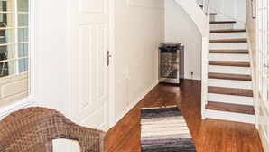 A hallway with a wooden floor, a white door, a wicker chair, a patterned rug, and a staircase with white railings. - 5 bedroom amazing home in Matre (Matre)
