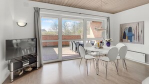 Ein modernes Wohnzimmer mit Flachbildfernseher, einem Esstisch mit Stühlen und einer großen Schiebeglastür, die auf eine Terrasse im Freien führt.
