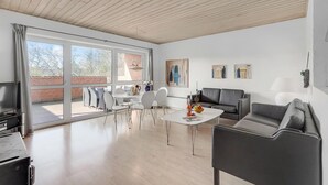 Ein großzügiger Wohnbereich mit einer großen SchiebeglasTür, die zu einer Terrasse im Freien führt, ein Essbereich mit weißem Tisch und Stühlen sowie eine Sitzecke mit einer Couch und Sesseln.