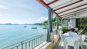 A seaside terrace with a view of the sea, a covered seating area, and a table with chairs.