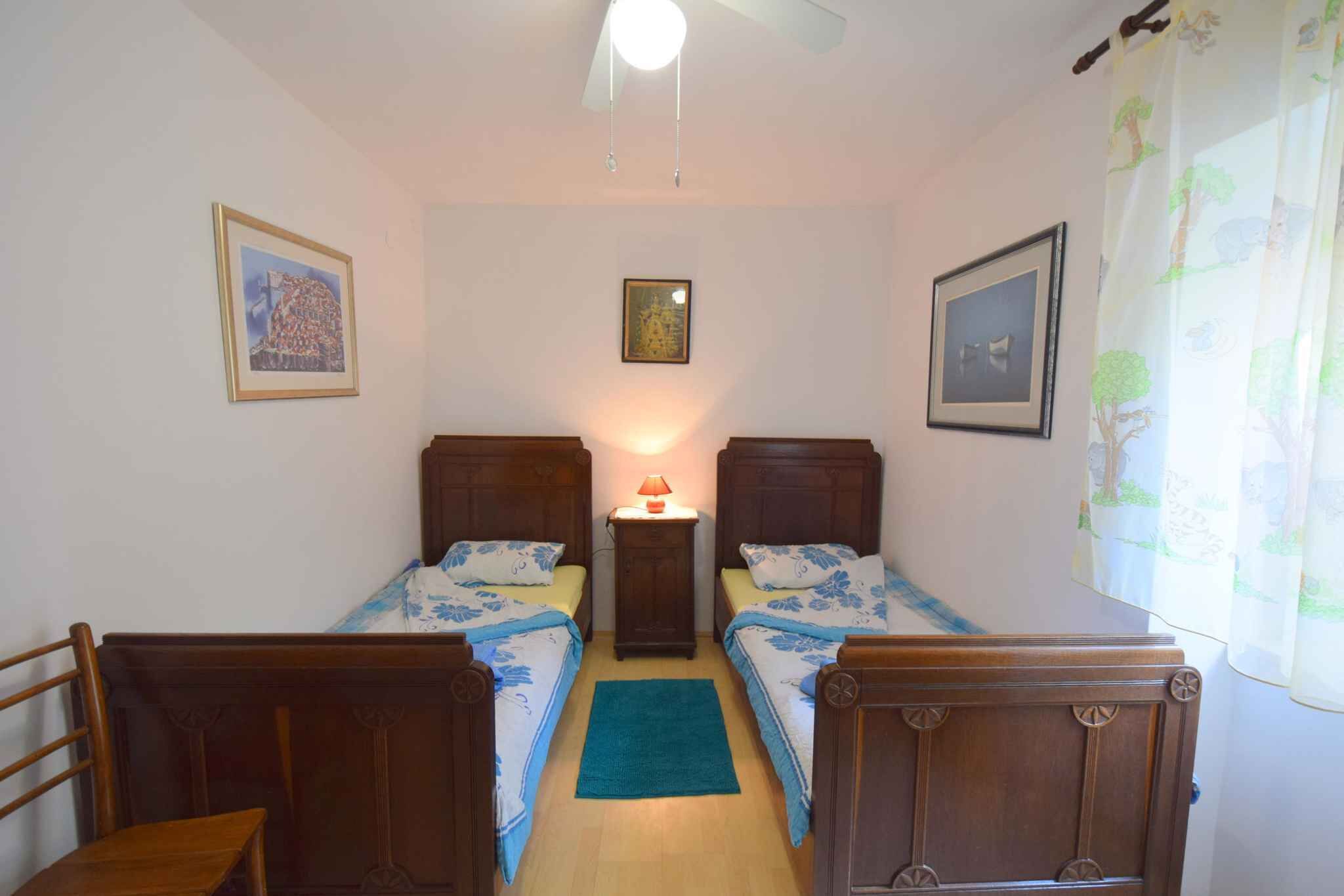 Une petite chambre à coucher accueillante, avec deux lits en bois, une table de chevet avec une lampe et un ventilateur de plafond.