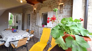 A covered patio with a table and chairs, a yellow chair, and potted plants.