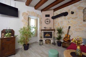 Un salon avec un mur en pierre, une cheminée, une horloge et une guitare.