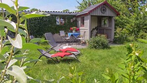 Une petite maison avec un jardin, une table avec des chaises et une nappe bleue.