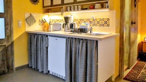Une cuisine compacte avec un plan de travail blanc, une machine à café et un grille-pain. Des placards sont situés au-dessus du plan de travail et un petit réfrigérateur en dessous.