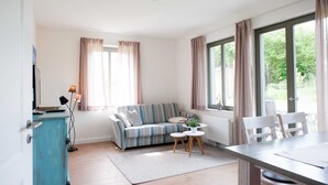 Ein modernes Wohnzimmer mit einem gestreiften Sofa, einem Esstisch mit Stühlen, einem kleinen runden Tisch mit Pflanze und einem Schrank.