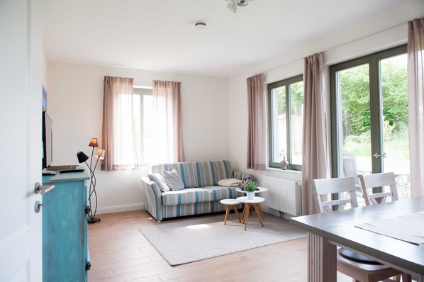 Un salon moderne avec un canapé à rayures, une table à manger avec des chaises, une petite table ronde agrémentée d’une plante et un meuble.