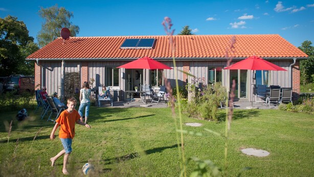 Ein Haus mit rotem Ziegeldach, einer Terrasse mit Gartenmöbeln und wolkenlosem, blauem Himmel.