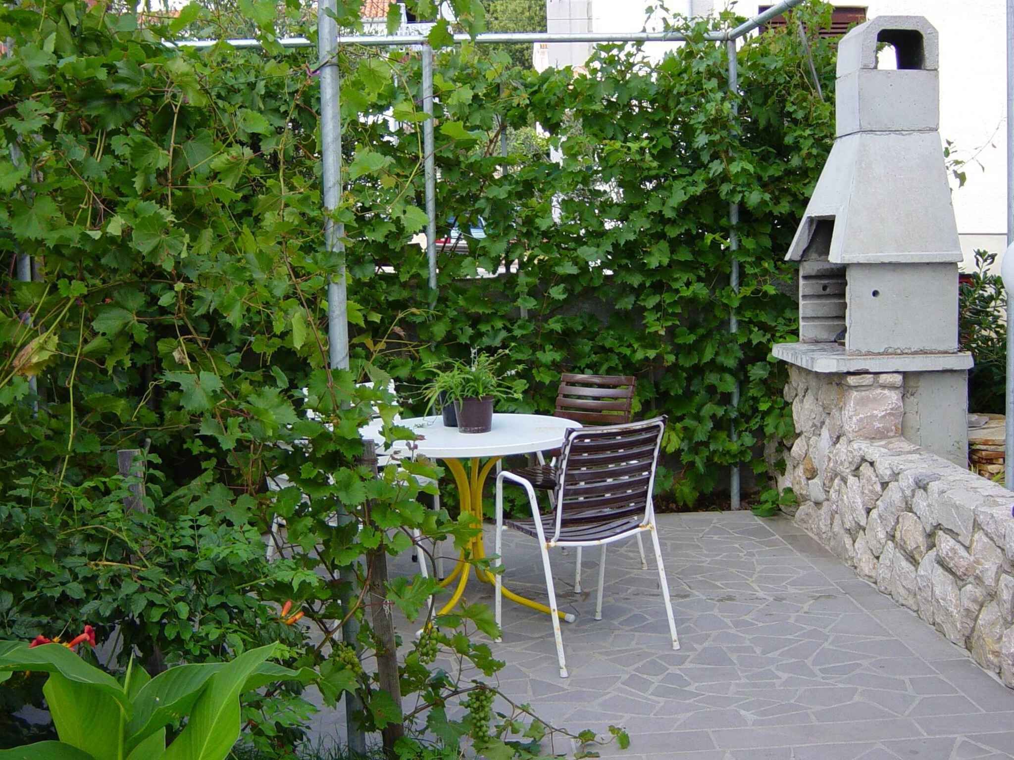Eine Terrasse mit rundem Tisch und zwei Stühlen, umgeben von üppigem Grün und einer Steinmauer.