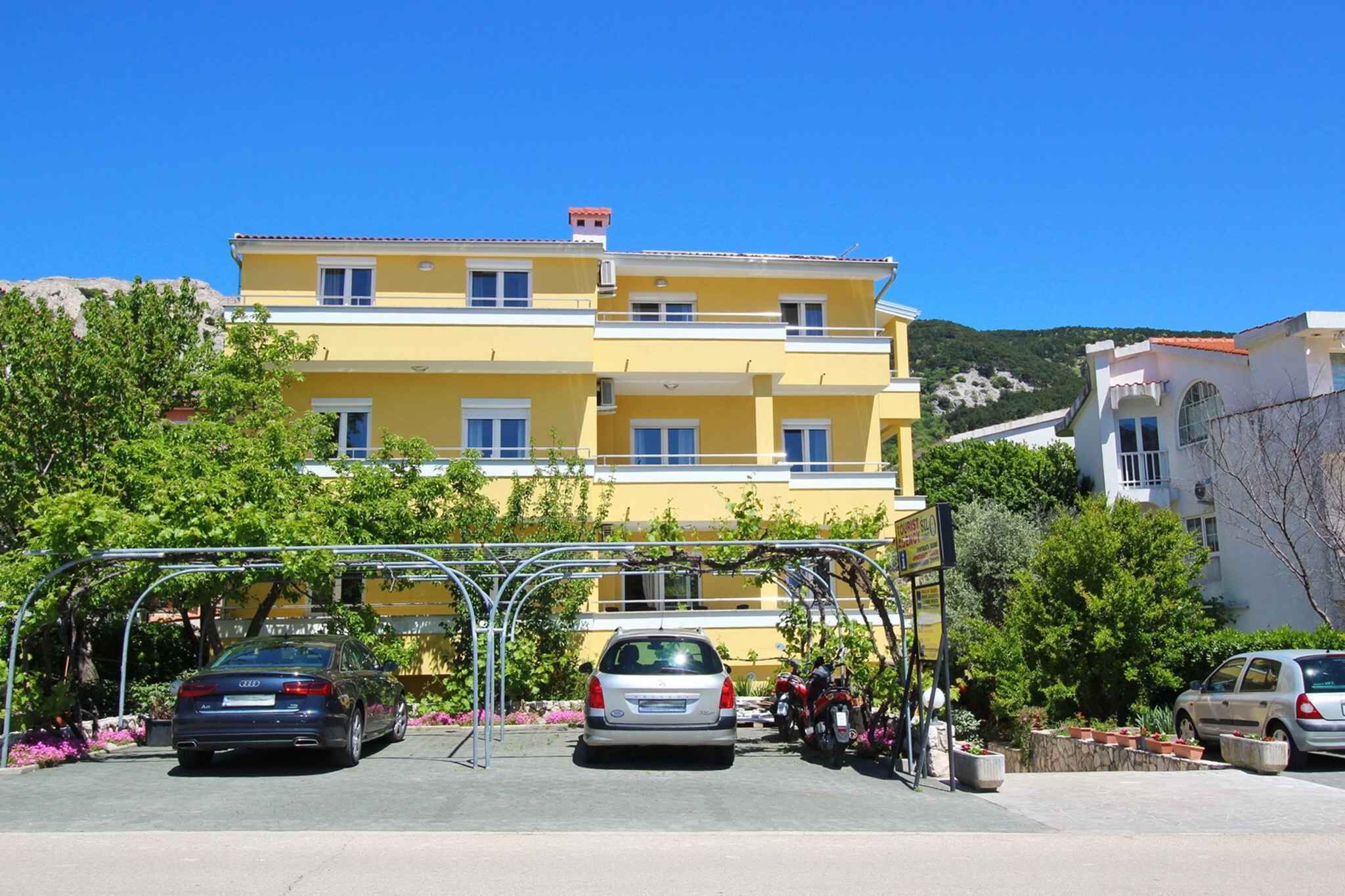 Un bâtiment jaune doté de nombreux balcons, avec des voitures garées et une structure en métal servant d’abri pour voitures.