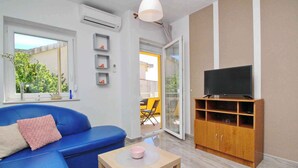 A modern living room with a blue sofa, a wooden TV stand, and a small table with a pink bowl. - Holiday apartment with balcony and air conditioning (Baška)