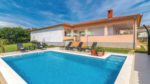 Una casa de dos pisos con piscina, mobiliario de exterior y jardín.