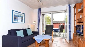 Een gemeubileerde kamer met een bank, een klein houten tafeltje, een stoel, een televisie en een boekenkast.