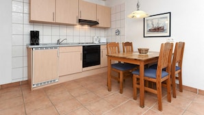 Een kleine keuken met houten kastjes, een eettafel met stoelen en een betegelde spatwand.