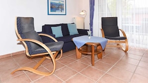 Een woonkamer met een bank, twee schommelstoelen, een bijzettafeltje en een lamp.